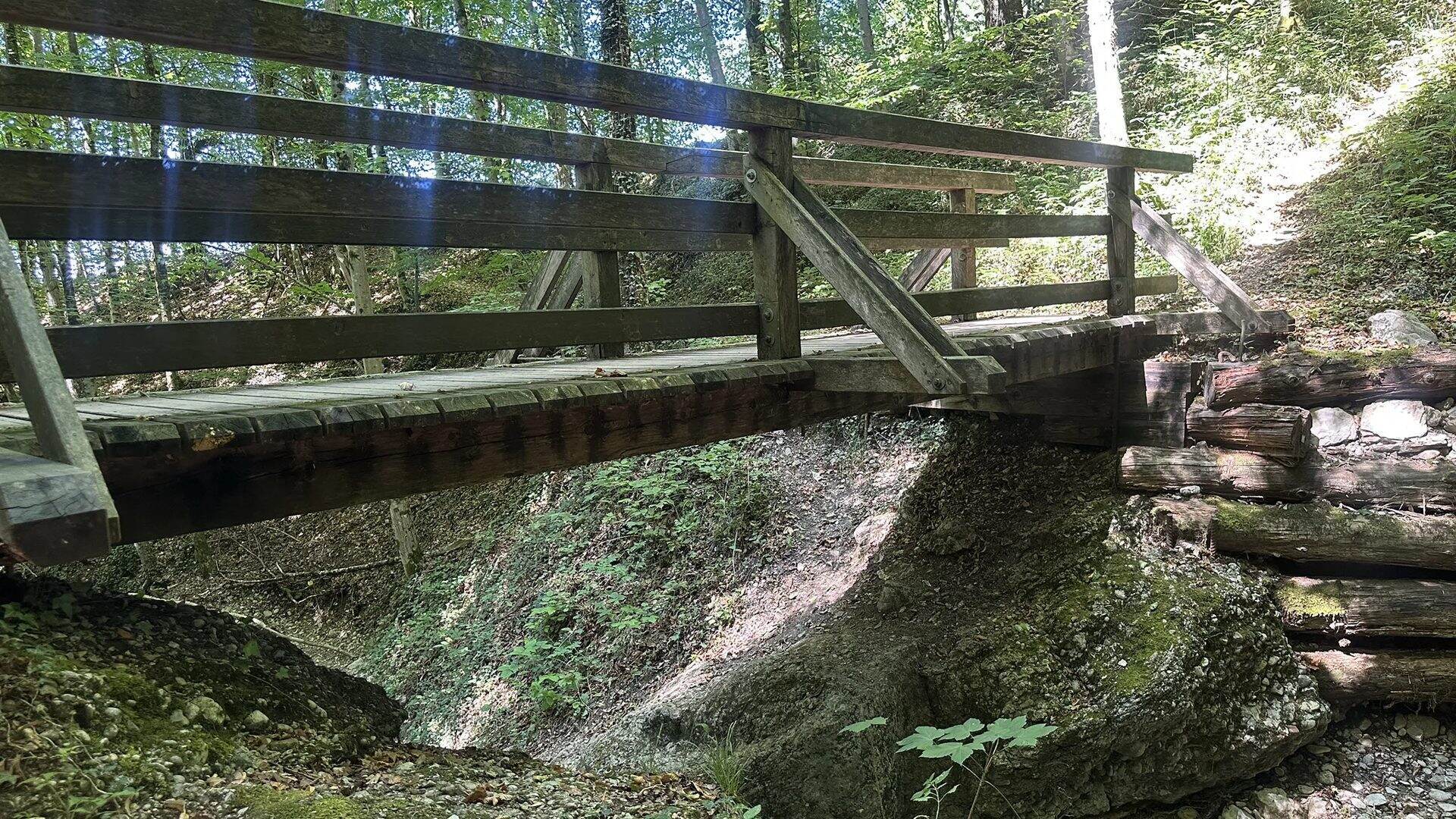 Hölzerne Fußgängerbrücke mit Geländer über dem Bachbett im Aigner Park
